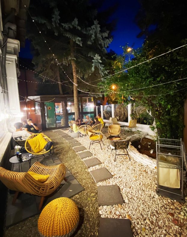 Grădina Cafenelei 9 seara, cu luminițe deasupra fotoliilor din rotin și pietriș alb